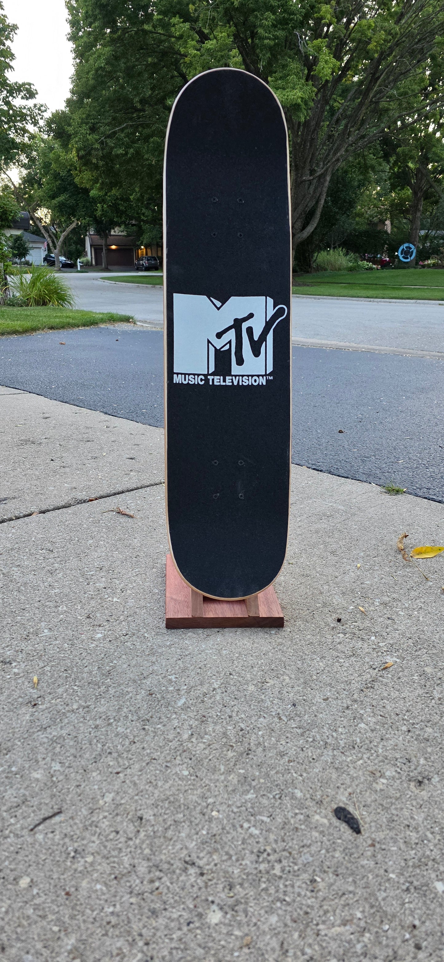 Little Claw holding a regular skateboard outside, displaying topside